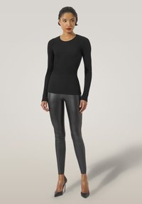 Schwarzes geripptes Langarmoberteil mit rundem Ausschnitt, kombiniert mit eleganten schwarzen Lederleggings und schwarzen High Heels, vor einem neutralen Hintergrund.