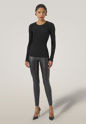 Maglietta nera a coste con maniche lunghe e scollatura tonda, abbinata a leggings in pelle nera e tacchi alti neri, su uno sfondo neutro.