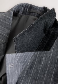 Blazer a righe grigie con collo in feltro, dotato di una fodera interna liscia. Il tessuto presenta una trama raffinata con materiali a contrasto sul collo.