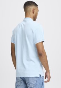 Svetlo modra bombažna polo majica s kratkimi rokavi, ovratnikom in stranskimi razpoki na robu, v kombinaciji z postarano modrimi jeans kratkimi hlačami.