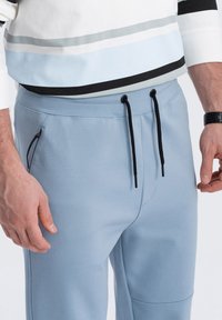 Lichtblauwe sweatpants van zachte stof, met een tailleband met trekkoord, een zijzak met rits en subtiele naaddetails.
