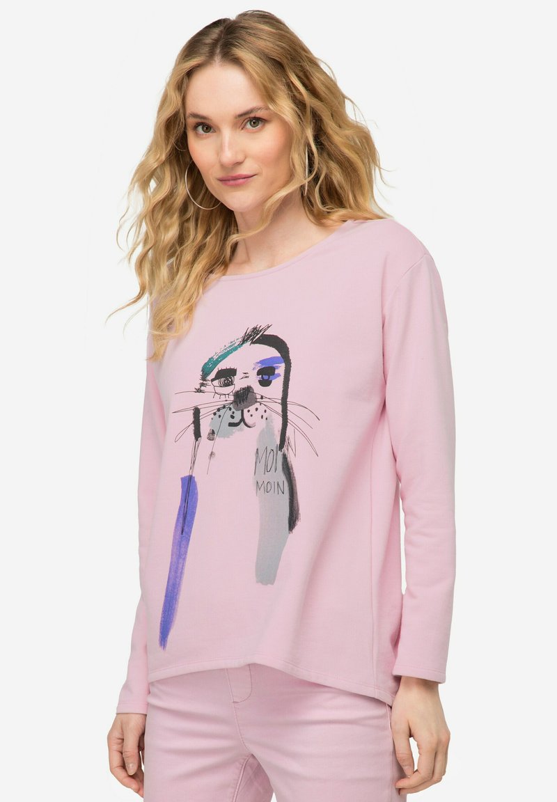 Lichtroze top met lange mouwen, featuring een speelse grafiek van een kat met artistieke penseelstreken in blauw en grijs. Zachte stoftextuur.