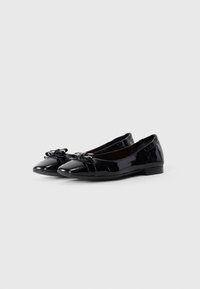 Sorte patent lær damers ballet flats med runde tåser og dekorative sløjfer på en hvid baggrund.