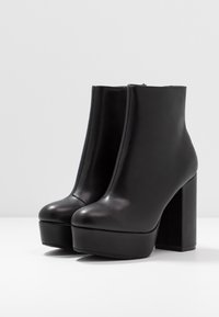 Botas de tobillo negras de cuero suave con una plataforma chunky y un alto tacón bloque, que presentan un diseño aerodinámico y bordes sin costuras.