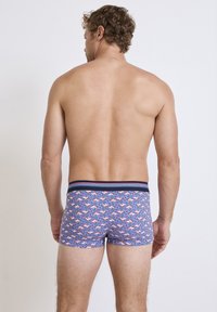 Bañador masculino de tejido en azul con un patrón de flamencos rosas. Cuenta con una cinturilla a rayas en contraste. Diseño de corte corto.