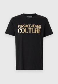 Melns kokvilnas t-krekls ar lieliem zelta burtiem, kas lasa "VERSACE JEANS COUTURE". Īsas piedurknes un apaļa kakla izgriezums. Vienkāršs dizains.