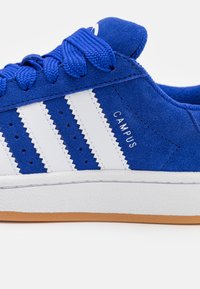 Μπλε σουέτ αθλητικά παπούτσια με λευκές δερμάτινες ρίγες, διαθέτουν υφασμένη λευκή ελαστική σόλα και κεντημένη ετικέτα "CAMPUS" στο πλάι.