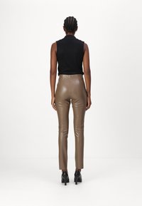 Top nero senza maniche abbinato a pantaloni aderenti in finta pelle marrone chiaro a vita alta. Scarpe col tacco nere completano l'outfit.