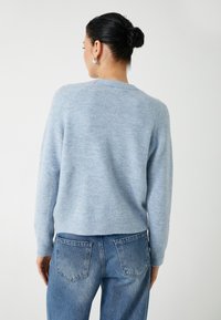 Hellblauer gestrickter Pullover mit rundem Halsausschnitt und Raglanärmeln, kombiniert mit blauen Jeans. Weiche Textur, gerippter Saum, lässige Passform.