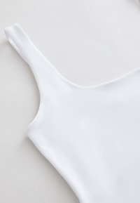 White sleeveless garment with a narrow strap and smooth fabric, laid flat on a light background.