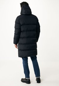 Abrigo de plumas negro con capucha, con acolchado horizontal, de largo prolongado y un ajuste relajado. Combinado con jeans azules y botas negras.