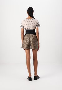 Top de manga corta beige con bordado negro, combinado con pantalones cortos de leopardo de cintura alta. Tela suave, diseño ajustado y estilo minimalista.
