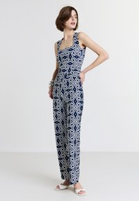 Tuta navy con un motivo geometrico bianco, con scollatura quadrata, spalline larghe e vita aderente che si apre in pantaloni a gamba larga.