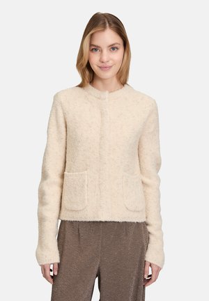 Cream-colored, textured jacket with a round neckline, two front pockets, and long sleeves, crafted from soft, fuzzy material.