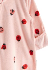 Vêtement en polaire rose pâle avec des motifs de coccinelles rouges et d'insectes noirs. La texture est douce et moelleuse, avec un détail de manches repliées.