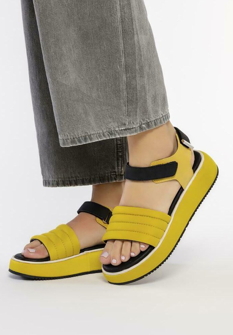 Sandalias de plataforma amarillas con dos correas anchas, acentos negros y una suela texturizada. Presenta un diseño voluminoso con una suela estratificada.