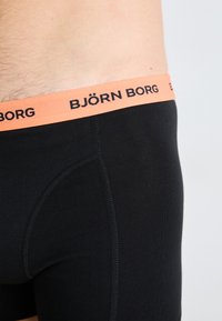 Black boxer briefs with an orange elastic waistband featuring "BJÖRN BORG" printed in black. Smooth texture and fitted design.