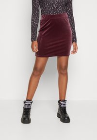 Minifalda de terciopelo malva con un diseño ajustado, combinada con botas de tobillo negras con cordones que presentan una suela gruesa y cordones blancos en contraste.