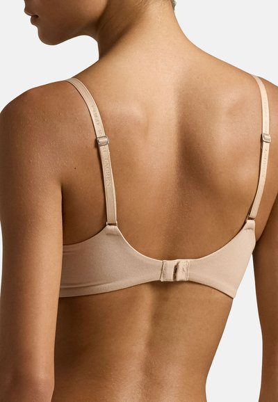 Reggiseno beige con spalline regolabili e chiusura a gancio sul retro. Tessuto liscio con un design senza cuciture. Texture morbida e stile minimalista.