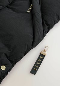 Duvet trapuntato nero con una texture liscia, dotato di un bottone a pressione dorato e un'etichetta con la scritta "BAKER" in oro su uno sfondo verde scuro.