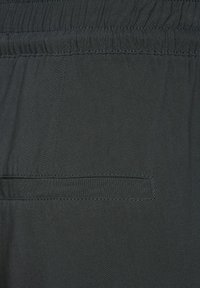 Tkanina w ciemnym kolorze z elastycznym pasem. Gładka tekstura z dyskretnym detalem w postaci kieszonki, podkreślona delikatnym przeszyciem.