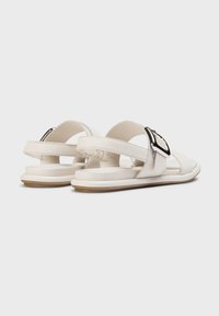 Sandales en cuir blanc avec une large sangle ornée d'une grande boucle métallique, design minimaliste, semelle plate et finition texturée subtile.