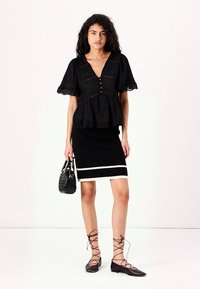 Black, short-sleeved top with a V-neck and button detail. Fitted black skirt with horizontal white stripe. Black accessories and shoes.