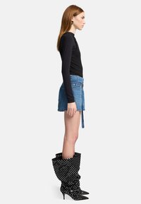 Maglietta nera a maniche lunghe, pantaloni shorts di jeans azzurri chiari con vita legata, e stivali neri al ginocchio con pois bianchi e punta affusolata.