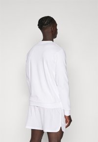 Sweatshirt blanc à manches longues et bords côtelés, associé à un short blanc. Texture lisse, sans motifs ni logos visibles.