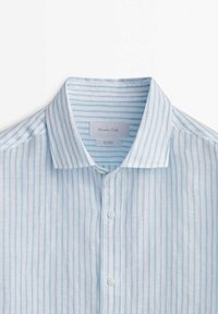 Chemise en lin rayée verticalement bleu clair et blanche avec un col pointu et des boutons sur le devant, étiquetée Massimo Dutti.