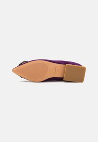 Escarpin en daim violet avec un talon carré, une pointe aiguë et des détails accentués. La semelle extérieure est beige avec des rainures texturées pour une meilleure adhérence.