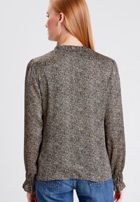 Blusa a maniche lunghe con scollatura a volant, sfondo scuro con motivo floreale chiaro e polsini elasticizzati. Tessuto texturizzato.