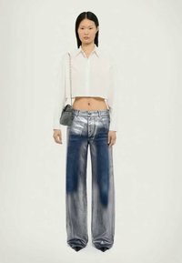 Jean large argenté-bleu avec une texture lisse, taille haute et détails décolorés. Assorti à une chemise blanche courte et un petit sac.