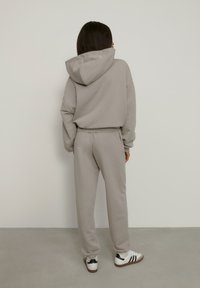 Svetlošedá mikina s kapucňou a zodpovedajúce teplákové nohavice z mäkkého materiálu. Má kapucňu a elastický pás, spárované s bielymi teniskami.