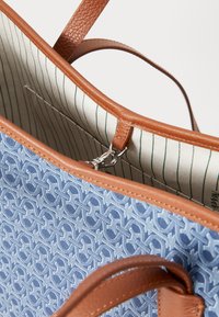 Blue patterned tote bag with brown leather accents. Features a striped fabric interior and a silver zipper for closure. Straps are also leather.