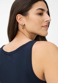 Canotta blu navy con scollatura rotonda, tessuto morbido e spalline sottili, indossata con orecchini a cerchio dorati visibili nell'orecchio.