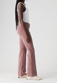 Jean évasé en velours côtelé rose pâle avec une taille haute et des poches avant, assorti à un débardeur blanc et des baskets blanches.