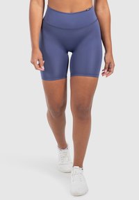 Marineblauwe hoge sportshorts met een gladde textuur en elastische tailleband. Witte sneakers met vetersluiting completeren de outfit.