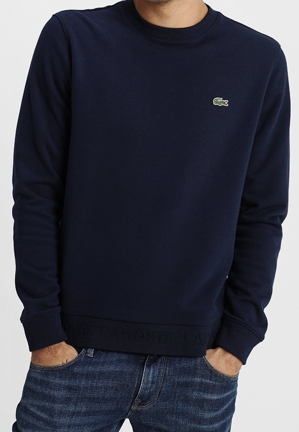 Granatowy sweatshirt wykonany z mieszanki bawełny, okrągły dekolt, ściągacze przy mankietach i u dołu, ozdobiony małym zielonym logo krokodyla po lewej stronie klatki piersiowej.