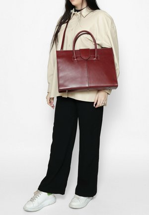 Rode leren handtas met een gestructureerd ontwerp, dubbele bovenhandvatten en een platte basis. Glad van textuur met minimale hardware en een centrale naad.