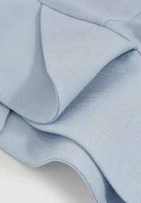 Tessuto blu chiaro con una trama testurizzata, che mostra pieghe morbide e curve lisce, rivelando una leggera lucentezza. Nessun motivo visibile o accessori.