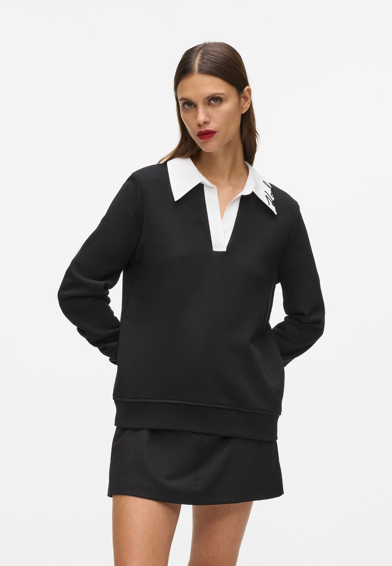 Sudadera negra con cuello blanco y media cremallera, con mangas largas y corte relajado. Detalles de logotipo en el cuello.