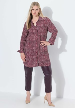 Burgunderfarbenes Button-up-Hemd mit vertikalem Streifenmuster, kombiniert mit eng anliegenden dunkelvioletten Lederhosen und nudefarbenen High Heels.