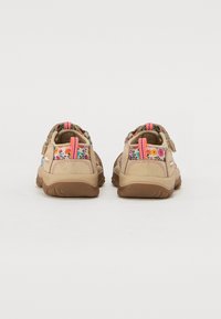 Vaaleat sandaalit, joissa on kukkakuosiset hihnat ja vaaleanpunaisia yksityiskohtia, varustettuna säädettävillä sulkimilla ja teksturoidulla kumipohjalla hyvän pidon takaamiseksi.