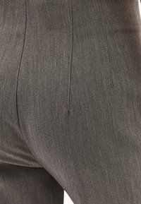 Pantalones gris a medida con una textura suave, pliegues marcados y un ajuste moderno. La tela tiene un ligero brillo y un sutil patrón de tejido.