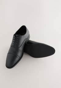 Schwarze Lederschuhe mit strukturierter Oberfläche, abgerundetem Zehenbereich und fünf Schnürlöchern, ausgestattet mit einer glatten Sohle und dezenten Ziernähten.