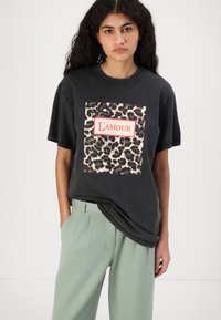Black oversized t-shirt featuring a leopard print design and red "L'amour" text. Smooth cotton fabric with short sleeves and a relaxed fit.