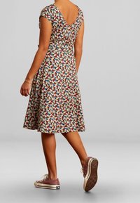 Šaty s květinovým vzorem, výstřihem do V, krátkými rukávy a rozšířenou sukní, doplněné o světlé růžové tenisky a viditelný řetízek na kotníku.