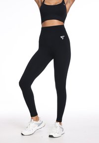 Zwarte high-waisted legging van rekbaar materiaal met een aansluitende pasvorm; heeft een subtiele logo op het heupgebied.