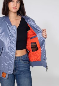Jasnoniebieska kurtka bomberka z pikowaną pomarańczową podszewką, zapinana na zamek z przodu, z kontrastowymi ściągaczami. Posiada metkę po wewnętrznej stronie lewej.